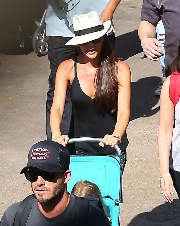 Victoria Beckham schiebt einen türkisfarbenen Trolley, während David Beckham neben ihr geht.