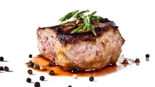 Ein gegrilltes Steak mit Rosmarin und Pfefferkörnern auf einem weißen Teller.