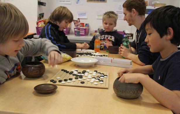 Eine Gruppe von Kindern spielt das Brettspiel Go an einem Tisch.