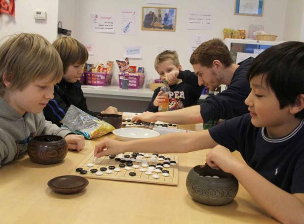 Eine Gruppe von Kindern und ein Erwachsener spielen das Brettspiel Go.