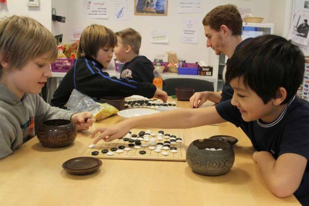 Eine Gruppe von Kindern spielt das Brettspiel Go an einem Tisch.