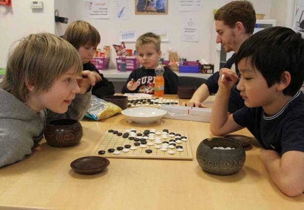 Mehrere Kinder und ein Erwachsener spielen das Brettspiel Go an einem Tisch.