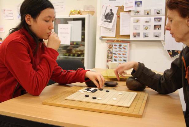 Zwei Personen spielen das Brettspiel Go an einem Tisch.