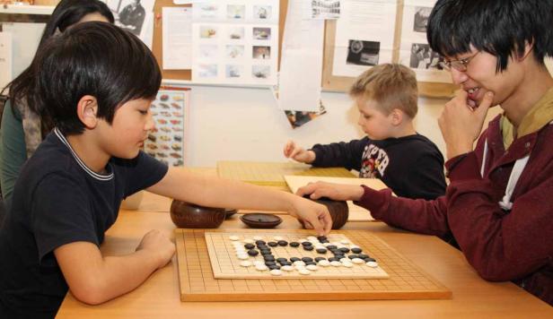 Kinder und ein junger Mann spielen das Brettspiel Go.