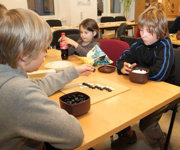 Kinder spielen das Brettspiel Go an einem Tisch.