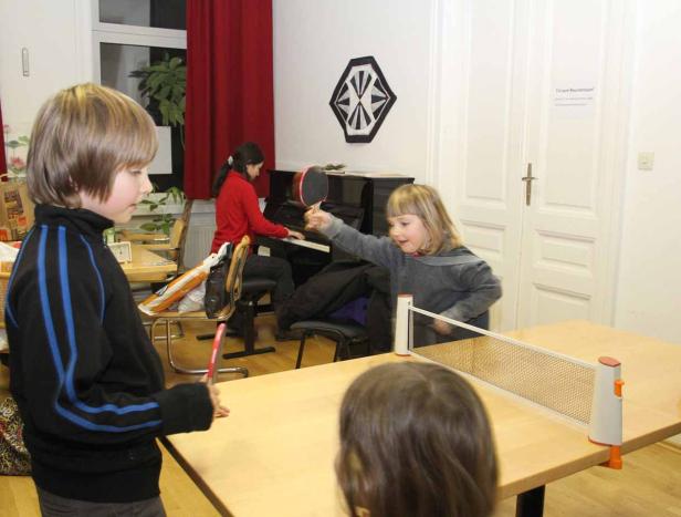 Kinder spielen Tischtennis, während ein anderes Kind Klavier spielt.
