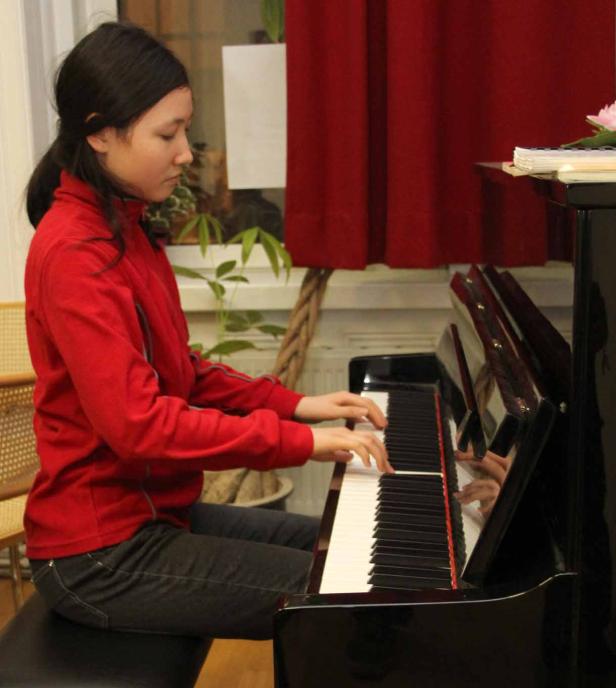 Eine junge Frau mit rotem Pullover spielt Klavier.