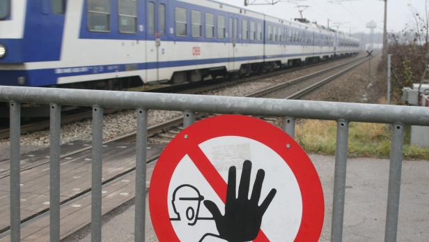 Ein rot-weißes Warnschild an einem Bahnübergang mit einem vorbeifahrenden Zug.