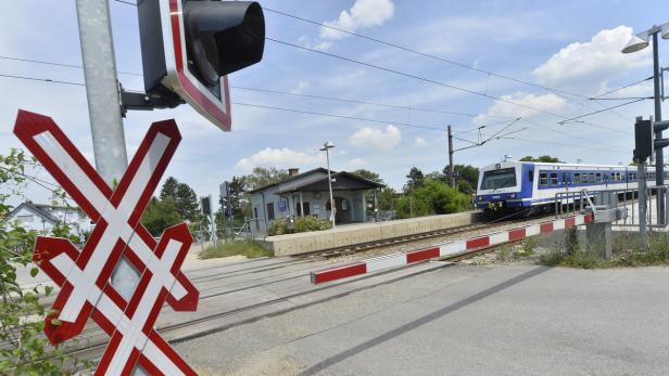 Ein blauer ÖBB-Zug nähert sich einem Bahnübergang mit Andreaskreuz.