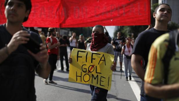 Eine Demonstrantin hält ein Schild mit der Aufschrift „FIFA Go Home!“ in einer Menschenmenge.