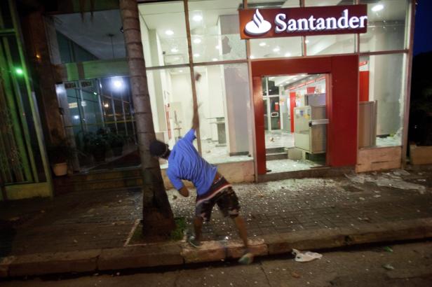 Ein Mann wirft einen Stein gegen die Scheibe einer Santander Bankfiliale.