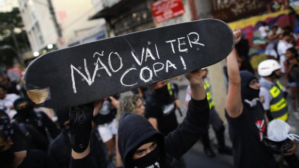 Eine Person hält ein Skateboard mit der Aufschrift „Não vai ter Copa!“ bei einer Demonstration hoch.