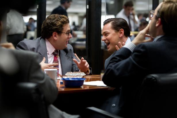 Jonah Hill und Leonardo DiCaprio gestikulieren lachend an einem Tisch.