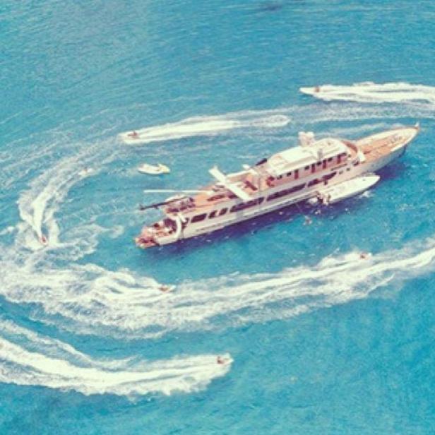 Eine große Yacht umgeben von mehreren Jetskis auf dem türkisfarbenen Meer.