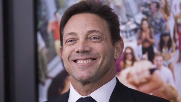 Jordan Belfort lächelt vor einem unscharfen Hintergrund mit Strandmotiven.