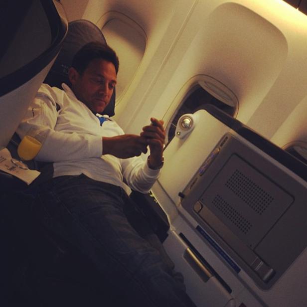 Ein Mann sitzt in einem Flugzeug und benutzt sein Handy.