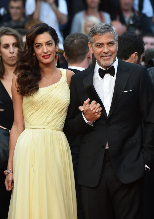 Amal und George Clooney halten Händchen auf dem roten Teppich.