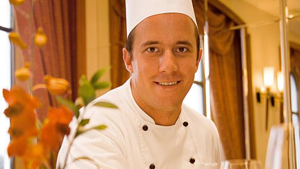 Ein lächelnder Koch in Kochuniform und Kochmütze.