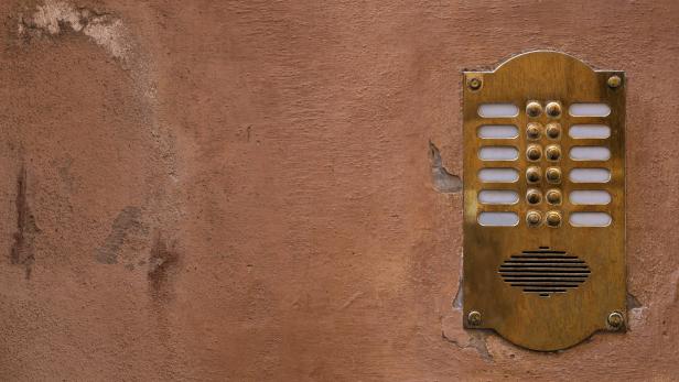 Old bronze intercom on an old wall with peeling paint. Ratio 16:9.