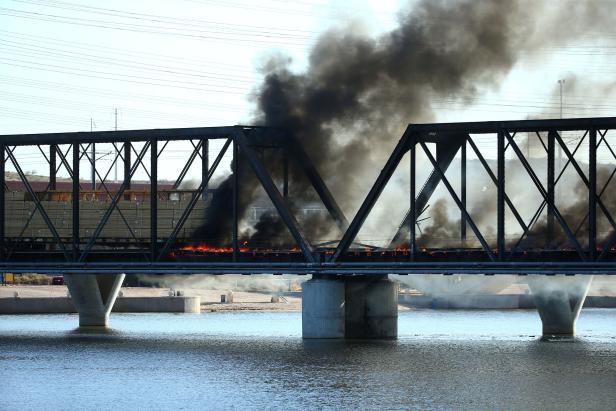 A derailed train burns over a portion of the bridge over Tempe Beach Park in Tempe