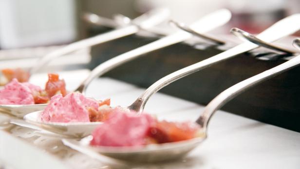 Silberlöffel mit rosa Mousse und Obst stehen in einer Reihe.