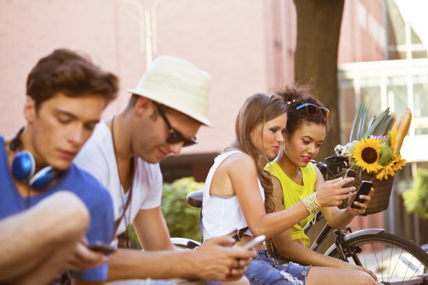 Eine Gruppe junger Leute sitzt im Freien und benutzt ihre Smartphones.
