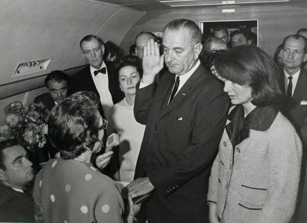 Johnson takes the presidential oath of office from Hughes as Bouvier Kennedy stands at his side aboard Air Force One at Love Field in Dallas