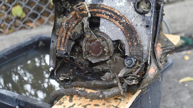 Eine beschädigte, schmutzige Maschine mit russischer Beschriftung liegt in einem Behälter.