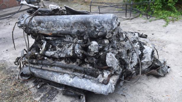 Ein zerstörter und verkohlter Automotor liegt auf dem Boden.