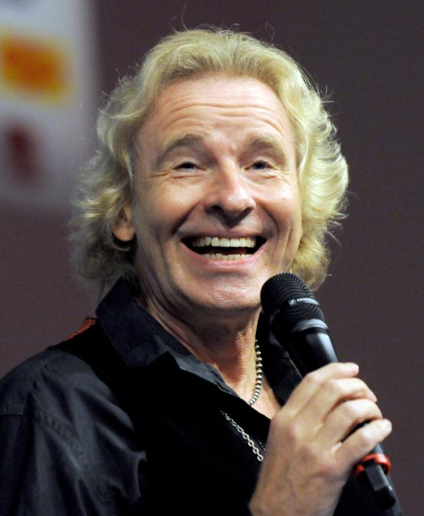 Thomas Gottschalk lacht und hält ein Mikrofon in der Hand.