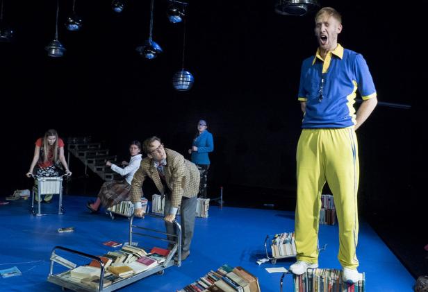 Auf einer Bühne stehen Schauspieler mit Bücherwagen.