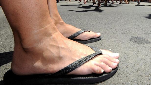 Nahaufnahme von Füßen in schwarzen Havaianas-Flip-Flops auf einer asphaltierten Straße.
