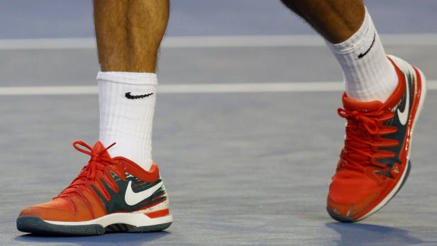 Nahaufnahme von Tennisschuhen der Marke Nike mit roten Schnürsenkeln und weißen Socken mit dem Nike-Logo.