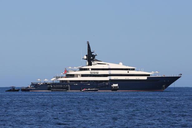 Eine große, mehrstöckige Yacht liegt auf dem ruhigen, blauen Wasser vor Anker.