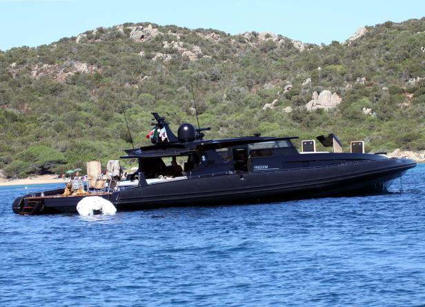 Eine schwarze Yacht namens „Freedom“ ankert vor einer bewaldeten Küste.