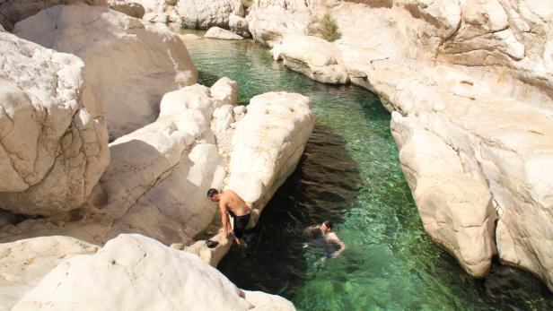 Zwei Männer schwimmen in einem Fluss zwischen hellen Felsen.