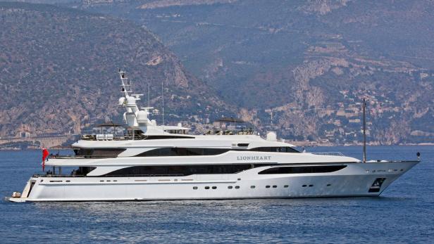 Eine große, weiße Yacht namens „Lionheart“ fährt auf dem Meer vor einer bergigen Küste.