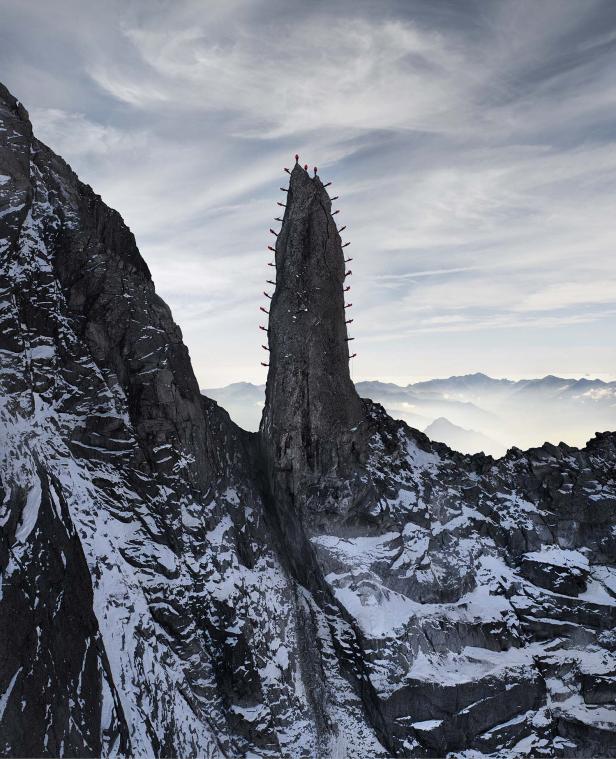 Kletterer steigen eine steile Felsnadel in einer verschneiten Berglandschaft hinauf.