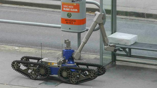 Ein Roboter mit Raupenketten hantiert an einer Bushaltestelle mit einem Paket in Wien.