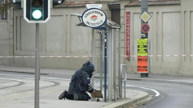 Ein Entschärfer kniet an einer Straßenbahnhaltestelle und untersucht einen Karton.