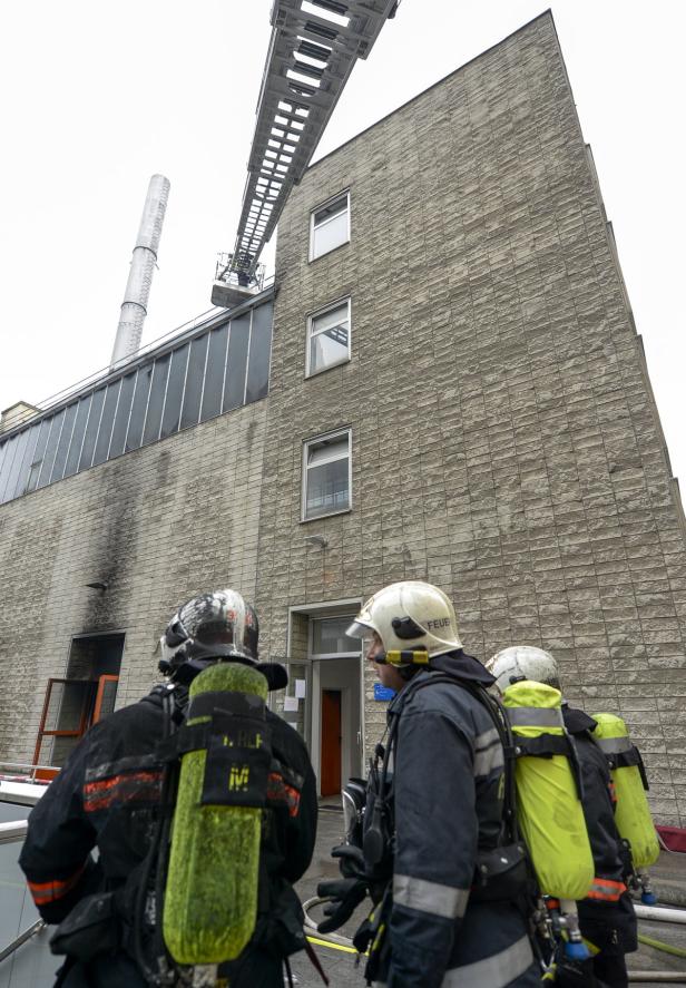 Feuerwehrleute stehen vor einem Gebäude, an dem eine Drehleiter angelehnt ist.