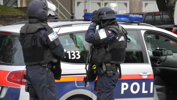 Zwei Polizisten in voller Montur stehen neben einem Einsatzwagen.