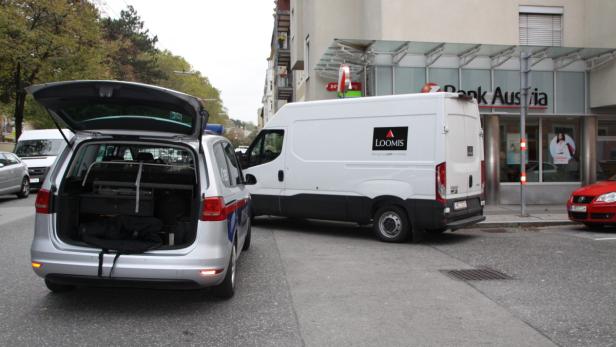 Ein Loomis-Geldtransporter steht neben einem Polizeiauto vor einer Bank Austria Filiale.