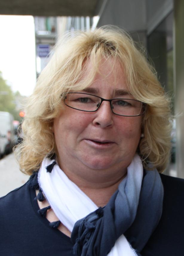 Eine Frau mit blonden, lockigen Haaren und Brille trägt einen Schal.