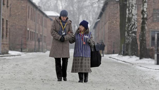 Eine Frau unterstützt eine ältere Dame in gestreifter Häftlingskleidung in Auschwitz.