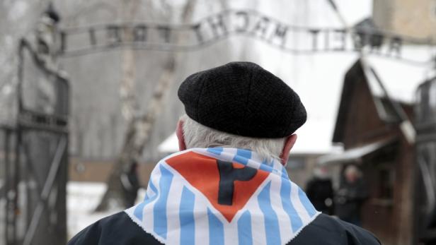 Eine Person mit einer gestreiften Schärpe steht vor dem Tor von Auschwitz.