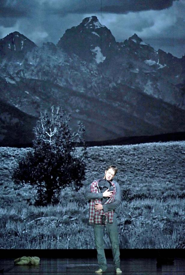 Ein Mann in Jeans und Hemd steht vor einer Bergkulisse.