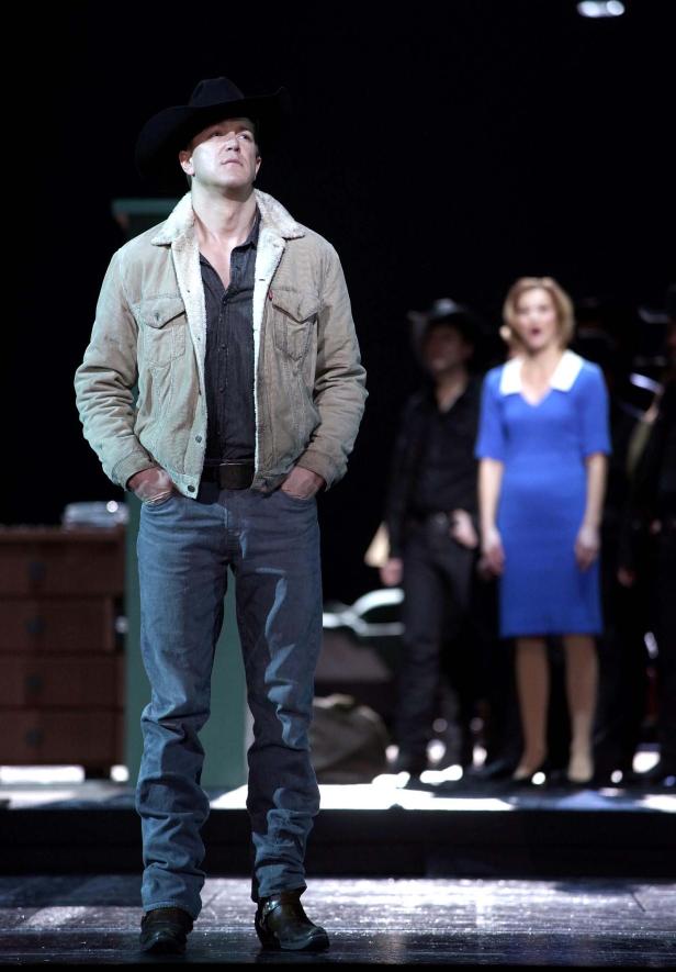 Ein Mann mit Cowboyhut, Jeansjacke und Cowboystiefeln steht auf einer Bühne.