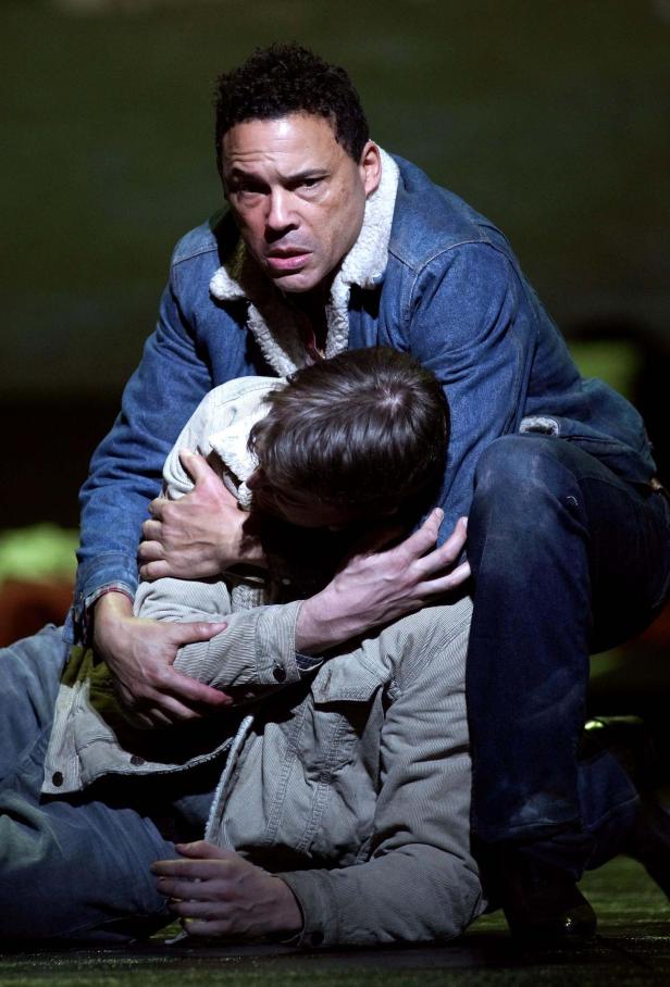 Ein Mann in Jeansjacke umarmt einen am Boden liegenden Mann.