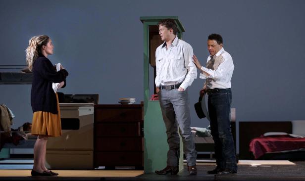 Szene aus einem Theaterstück mit drei Schauspielern in einem spartanischen Raum.